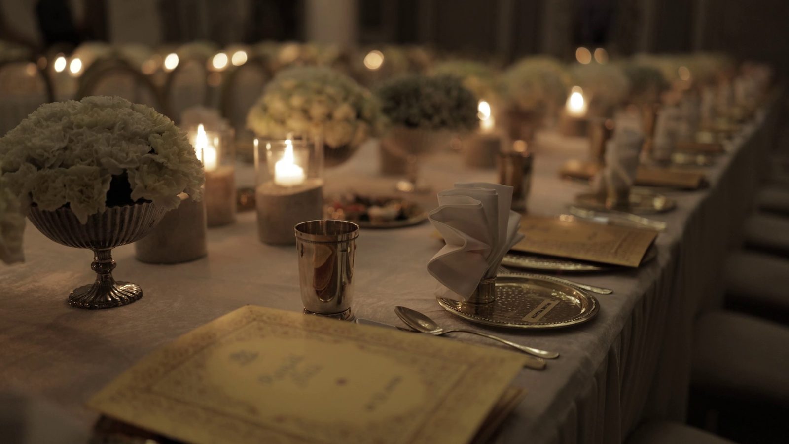 A place setting with white florals, a silver beaker, a folded napkin and a menu card out of focus.