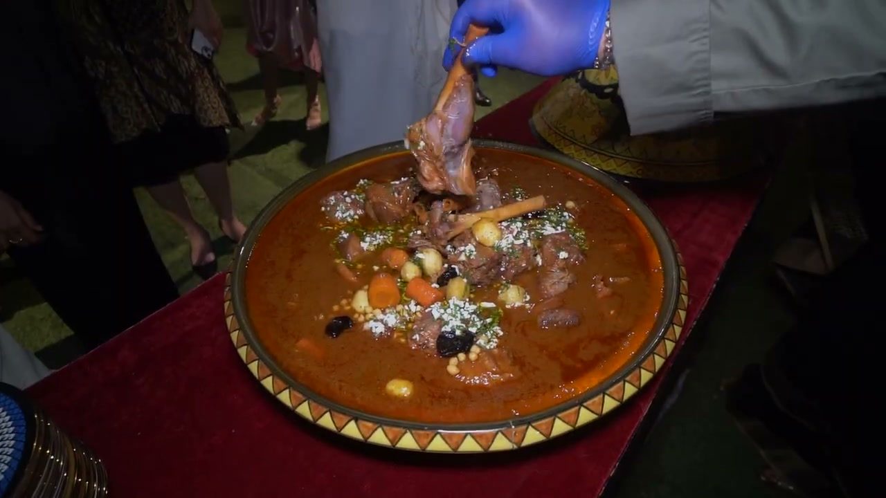 A brass tray of slow-cooked meat, vegetables and dried fruit, being served.