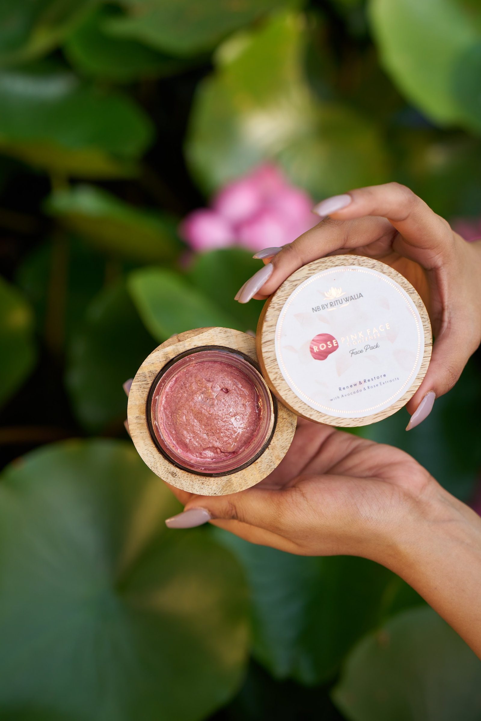 An open jar of Rose Pink face pack held in two hands against leaves, the paste's texture visible.